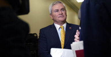 Representative James Comer in a dark suit and yellow tie with members of the media