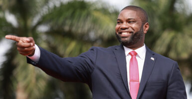 Byron Donalds wears a dark grey suit and red necktie as he smiles.
