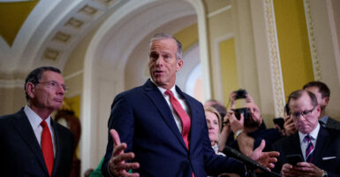 John Thune gestures, wearing a dark blue suit and red necktie.