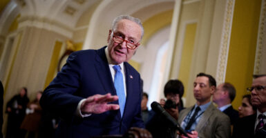Chuck Schumer stands wearing a dark blue suit and a light blue necktie.