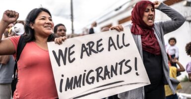 Two women shout as they hold signs protesting.
