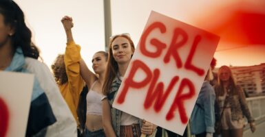A college-aged woman holds a sign that says, "GRL PWR".