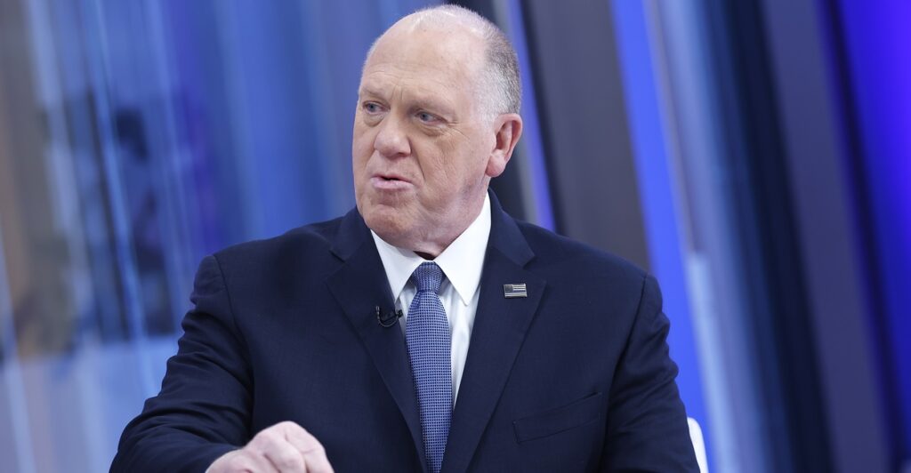 Tom Homan sits while discussing the border and emphasizes his point by pointing with his right hand.