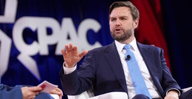 JD Vance raises his right hand as he sits and talks during an interview.