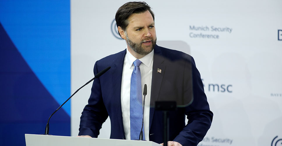 Vice President JD Vance stands at the podium in a blue suit at the Munich Security Conference.