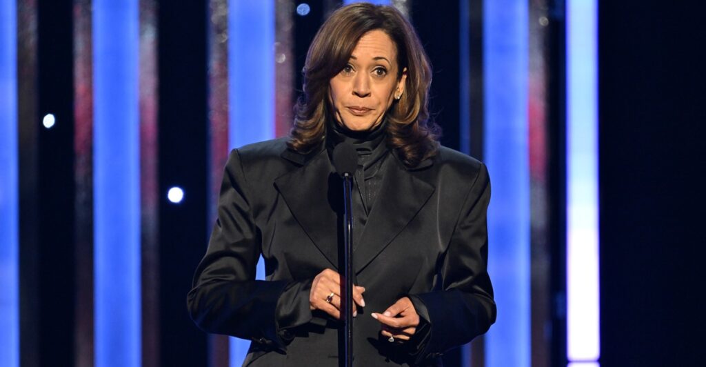 Kamala Harris stands up on stage during an awards ceremony wearing a black outfit.