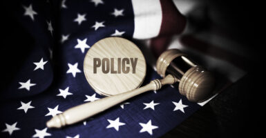 A judge's gavel rests on an American flag, alongside a round wooden disc with the word "policy" written on it.