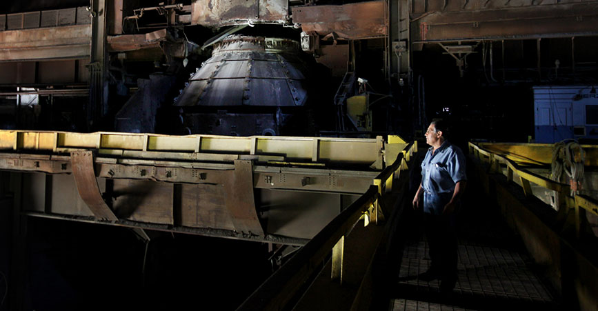 A man stands in a steel plant overlooking idled machinery.