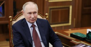 Vladimir Putin sits in a chair looking straight ahead with his arms by his side.