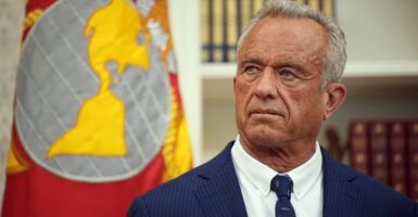 Robert F. Kennedy stands and listens to Donald Trump with his head turned slightly to his right.