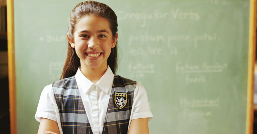 A school girl in a uniform poses for a photo while standing.