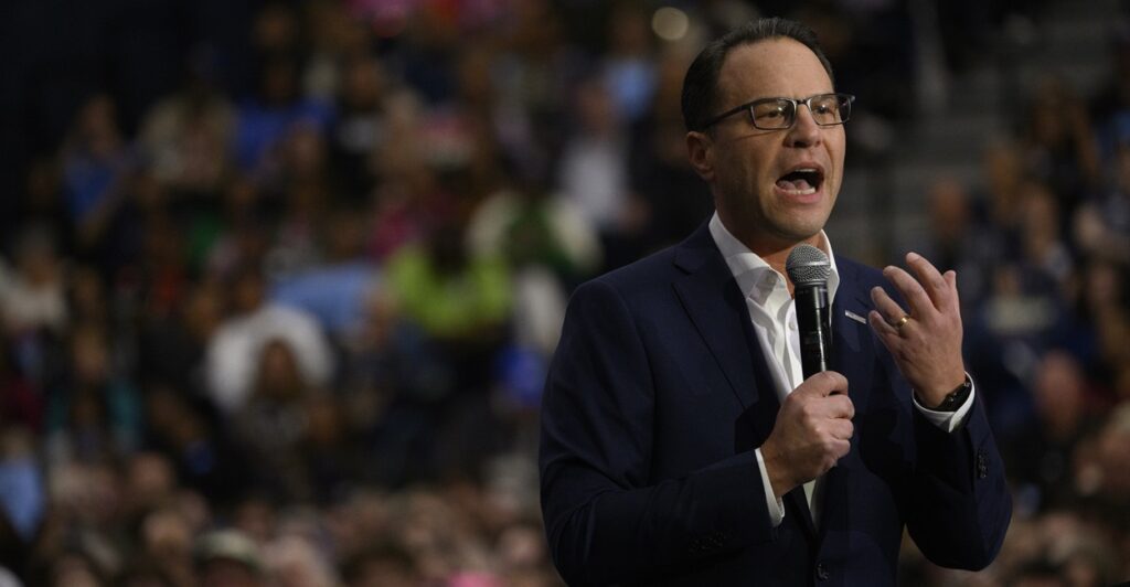 Josh Shapiro stands while holding a microphone as he talks during a rally.