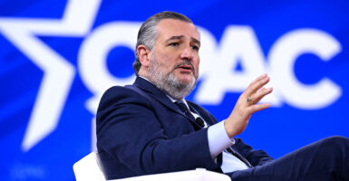 Ted Cruz in a blue suit sits in front of a CPAC logo