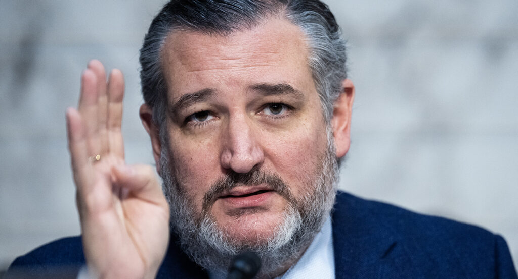 Ted Cruz in a suit holds up his hand