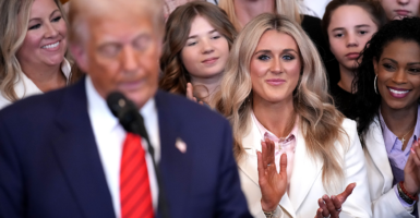 Trump reads from a podium as Riley Gaines and other female athletes applaud behind him.