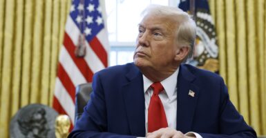 Donald Trump sits at a table with his hands set in front of him while he looks to his right.
