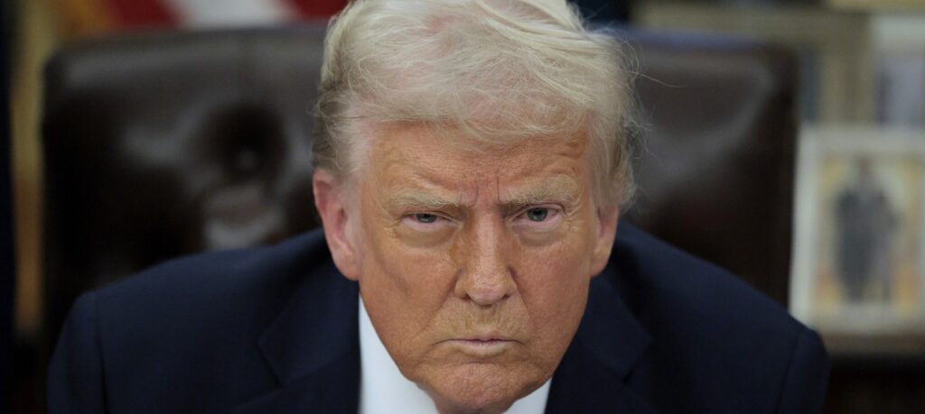 Donald Trump sits at his desk in the White House and glares ahead.