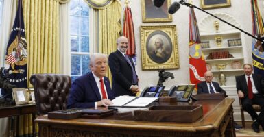 With microphones around him, Donald Trump sits at his desk and talks to reporters.