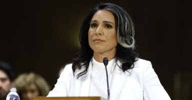 Tulsi Gabbard sits with a microphone in front of her and looks ahead.