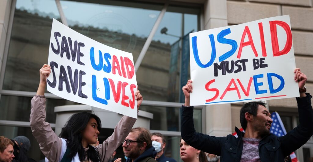 A man and a woman hold up signs saying that USAID must be saved while standing in front of a building.