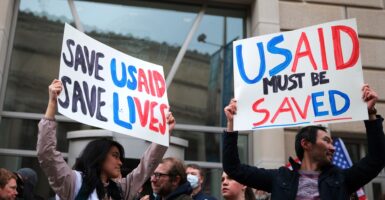 A man and a woman hold up signs saying that USAID must be saved while standing in front of a building.