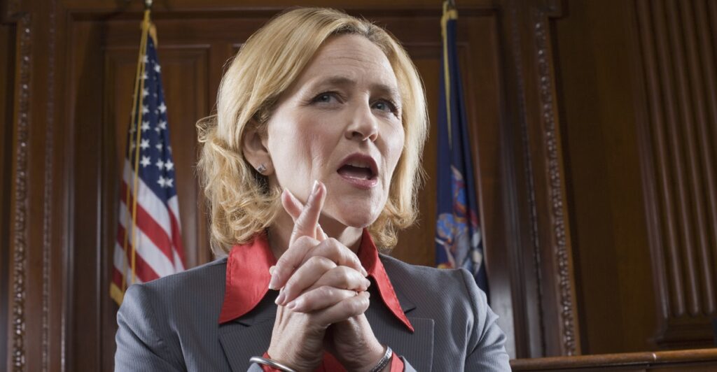 A female lawyer clasps her hand together as she talks in court.