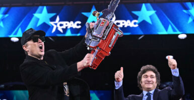 Elon Musk (L) holds a chainsaw high that Argentine President Javier Milei (R) gave him to represent how he’s cutting government.