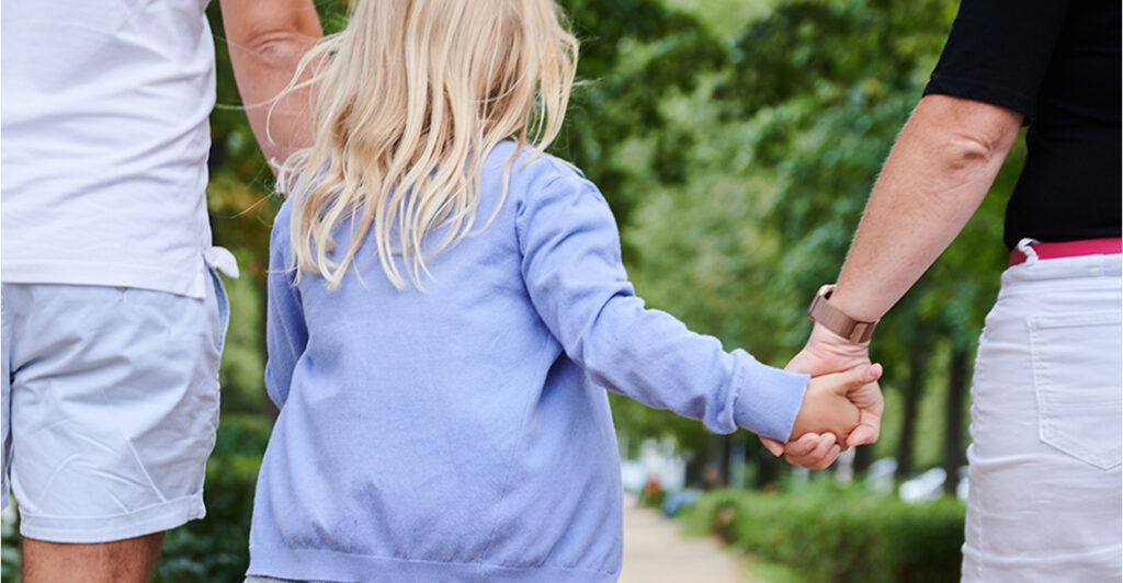 A mom and dad hold their daughter's hand on a walk.