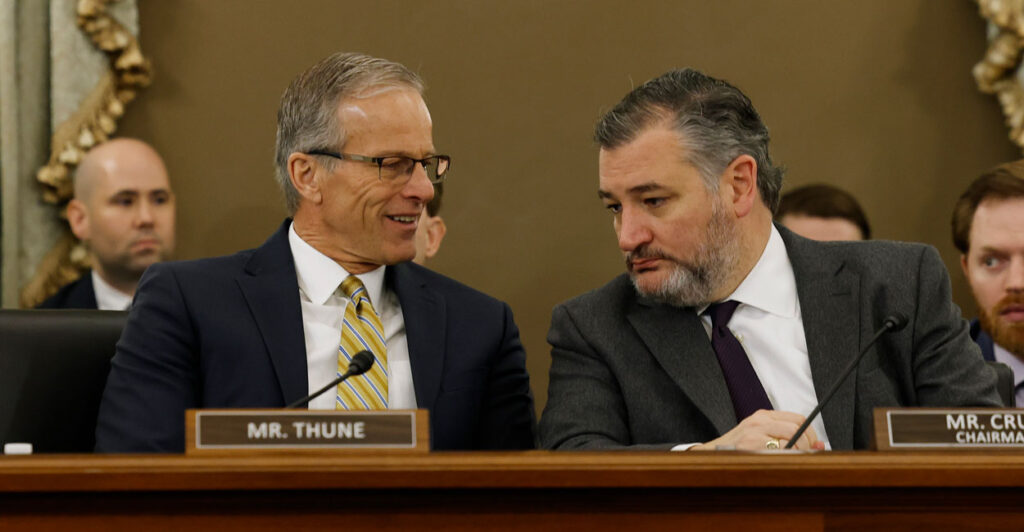 Senators John Thune and Ted Cruz in suits speaking to each other at a Senate hearing