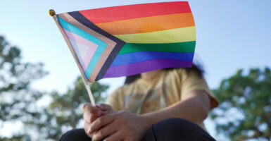 a young person sits with a transgender flag in hand at an angle that covers his face