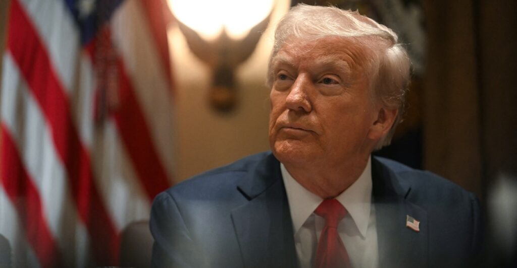 Donald Trump sits at his desk at the White House and looks to his left.