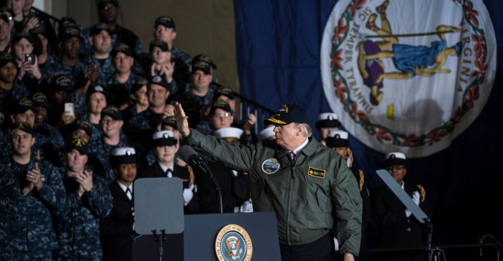 President Donald Trump waves after speaking to Navy and shipyard personnel aboard the nuclear aircraft carrier Gerald R. Ford at Newport News Shipbuilding in Newport News, Va., eight years ago this month on March 2, 2017. A large Virginia state flag hangs vertically on the wall at right.
