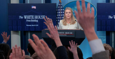White House press secretary Karoline Leavitt fields questions at a news conference, with reporters raising their hands to be called upon.