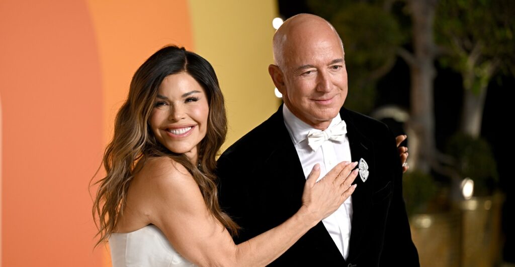 Jeff Bezos stands on a red carpet as his wife Lauren Sanchez puts her right hand on his chest.