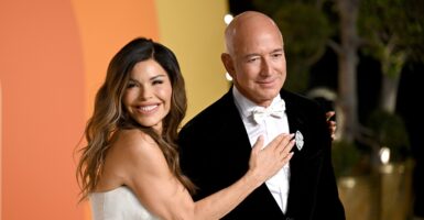 Jeff Bezos stands on a red carpet as his wife Lauren Sanchez puts her right hand on his chest.