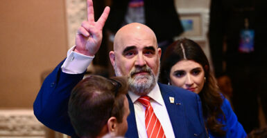 Chris LaCivita in a blue suit with a red tie makes a V for victory symbol