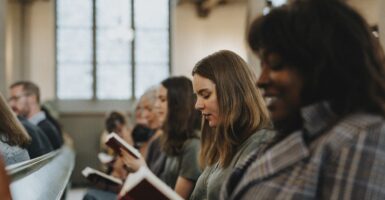 Women are sitting in a pew while reading a hymn book in a religious facility.