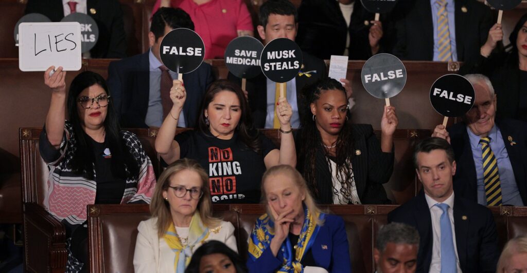 Democrats sit in seats and hold up signs protesting Donald Trump's speech.
