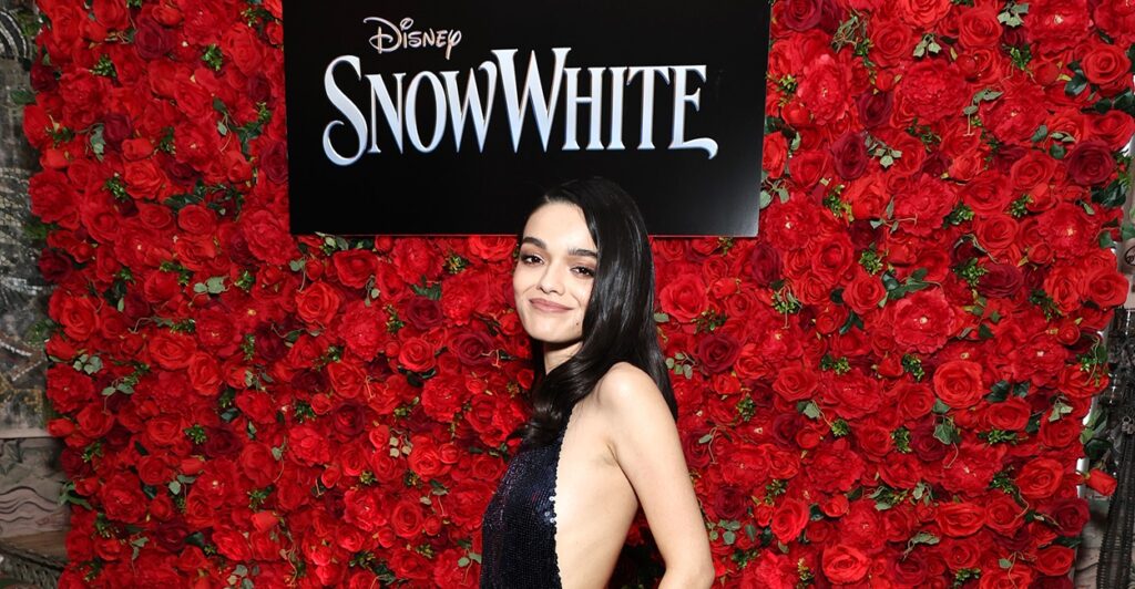 Rachel Zegler stands in a black dress in front of a Snow White sign on the red carpet.