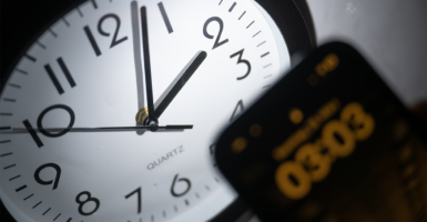 A smartphone displays the time as 03:03, while on an analog clock on a wall, it's still 02:03. The difference is due to Daylight Saving Time.