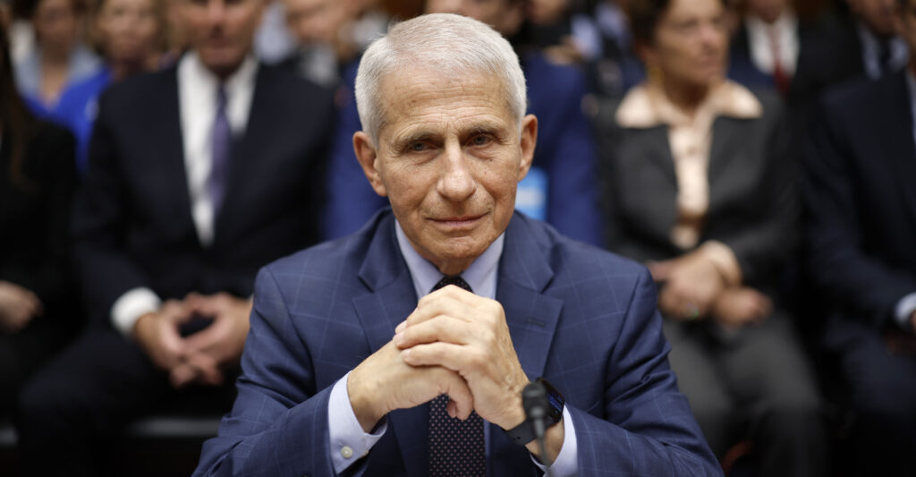 Anthony Fauci wears a blue suit as he sits with his hands clasped.