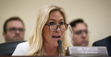 Marjorie Taylor Greene wears a white suit and black-rimmed glasses.