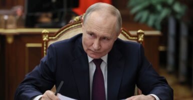 Vladmir Putin wears a black suit and necktie as he sits.