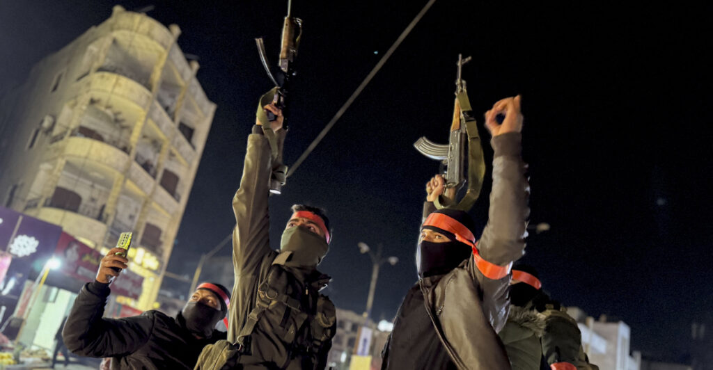 Masked armed forces of the new Syrian government raise their Kalashnikov rifles as they are being deployed to the coastal city of Latakia.