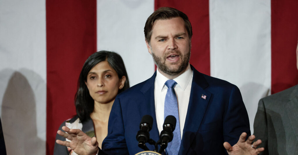 Vice President JD Vance and wife Usha Vance with the red and white stripes of a large U.S. flag as backdrop