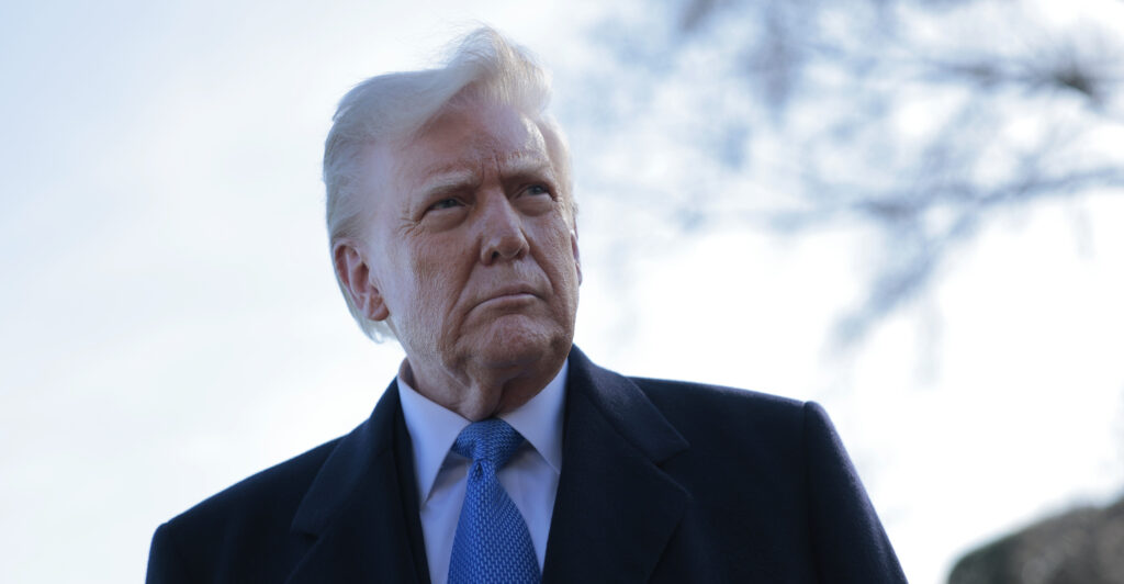 Donald Trump is outside wearing a black coat and light-blue necktie.