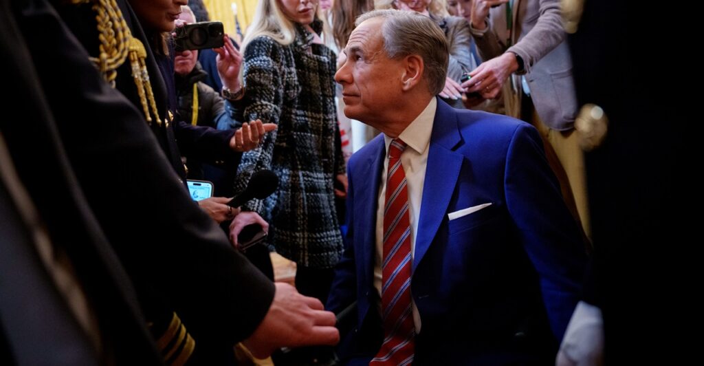 Greg Abbott is surrounded by a crowd as he looks up at a person.