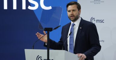 JD Vance stands at a podium with a microphone in front of him and talks while he raises his right hand.