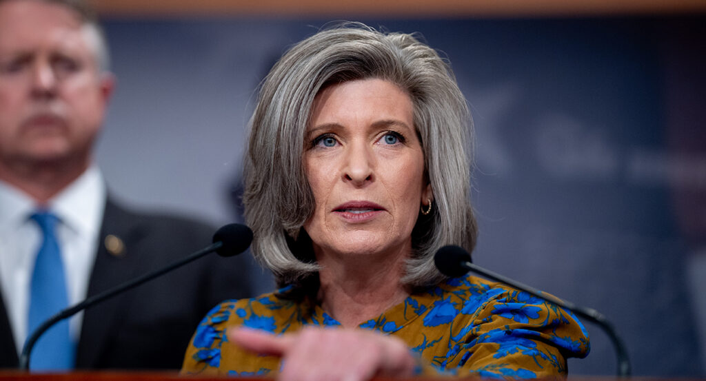 Joni Ernst in a red and blue blouse looking livid