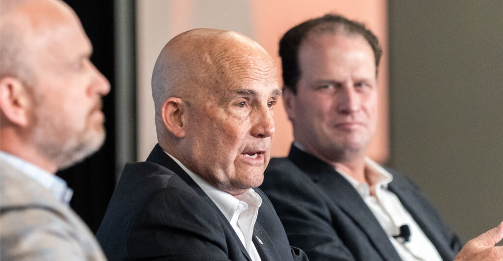 Rep. Keith Self wearing a black suit and speaking next to Dr. Kevin Roberts and Rep. August Pfluger.